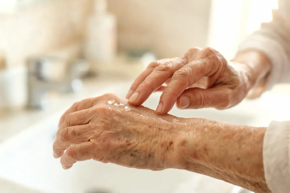 Older woman's hands applying a light cream to the back of the hand